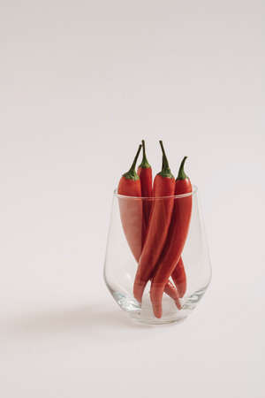 Red chili peppeprs in a transparent glass stand on a white background, vertical composition with copy spaceの写真素材