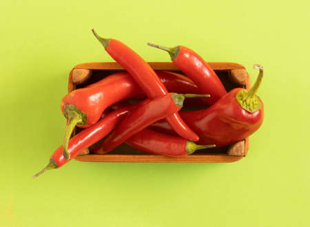 Red chili peppeprs in a wooden box lay down on a pastel green background, flat lay composition