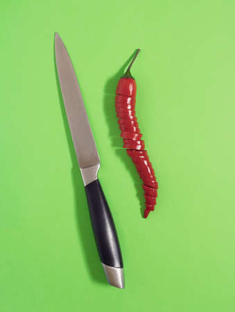 Kitchen knife and sliced red chili peppepr lay down on a pastel green background, flat lay minimalistic conceptの写真素材