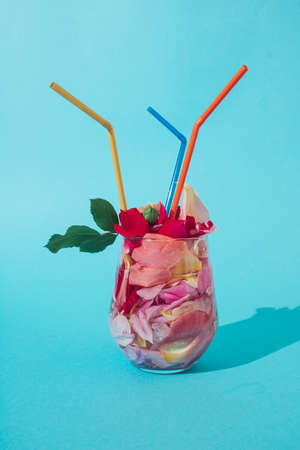 Cocktail of rose petals in a glass with straws. Summer composition on blue backgroundの写真素材