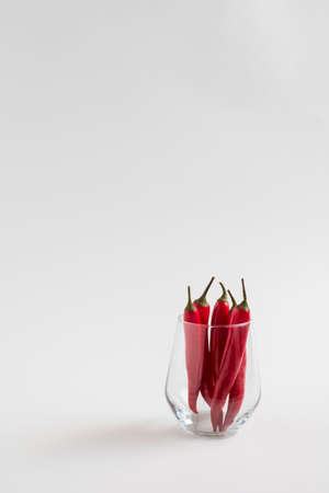 Red chili peppeprs in a transparent glass stand on a white background, vertical composition with copy spaceの写真素材