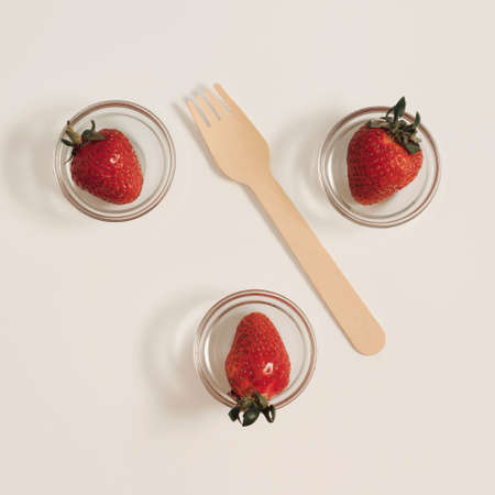 Ripe red strawberries in transparent glass pots and wooden fork lay down on white background. Flat lay summer refreshing conceptの写真素材