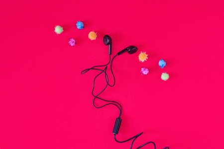 Music comes out from earphones. Minimal entertaiment concept, flat lay composition on pastel red...