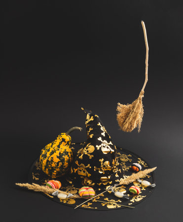 Floating witchÂ´s broomsstick, pumpkin, little fabric pumpkinks and candys standing on witchÂ´s hat. Funny Halloween minimal decoration concept on black backgroundの写真素材