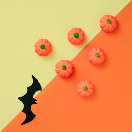 Little rubber pumpkins and fabric bat  lay down on yellow and orange background. Square geometric flat lay composition, autumn halloween celebration conceptの写真素材
