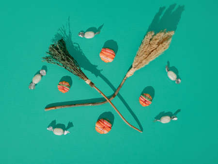 WitchÂ´s broomssticks, little fabric pumpkins and candies lay down on cyan background. Flat lay...