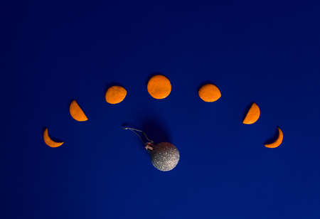 Lunar phases made of tangerine peel and decorative ball like Earth lay down on dark royal blue background. Flat lay horizontal composition, funny astronomical Christmas or New Year celebration conceptの写真素材