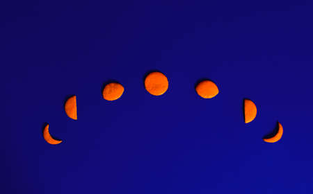 Lunar phases made of tangerine peel lay down on dark royal blue background. Flat lay horizontal composition, funny astronomy decorative conceptの写真素材