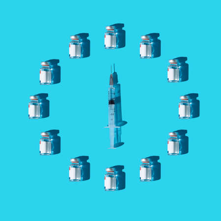Clock made of vaccine vials and syringe. Minimal flat lay composition on cyan background, global booster dose imunization conceptの写真素材