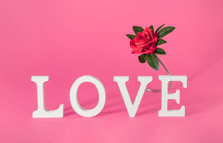 Word LOVE written in wooden letters with red rose. Horizontal composition on pastel pink background. Minimal romantic Valentines or International Women's day vintage conceptの写真素材