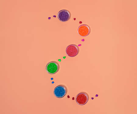 Colored coconut crumbs in a glass bowls. Flat lay square composition on pink coral background, minimal colorful Holi celebration conceptの写真素材
