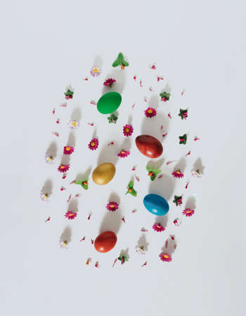 Easter eggs, spring flowers and leaves on white background. Vertical flat lay composition, egg shape pattern, minimal Easter celebration conceptの写真素材