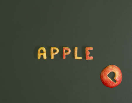 Letters cut from fresh apple on a dark green background. Flat lay horizontal composition, healthy food conceptの写真素材