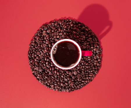 Cup of black coffee and coffee beans in circle on red background. Minimal horizontal flat lay composition, coffee culture conceptの写真素材