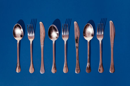 Set of spoons, knives and forks on a blue background. Minimal horizontal flat lay composition, food serving conceptの写真素材