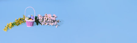 Easter eggs in basket and spring tree branches on bkue gray background. Minimal horizontal...