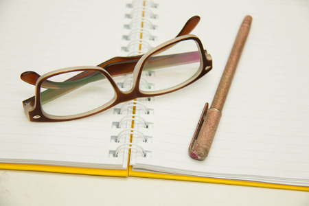 Ballpoint ink writing pen ready for taking notes on a spiral bound study and composition notebook open to a blank ruled paper sheet with reading glasses over white.の写真素材