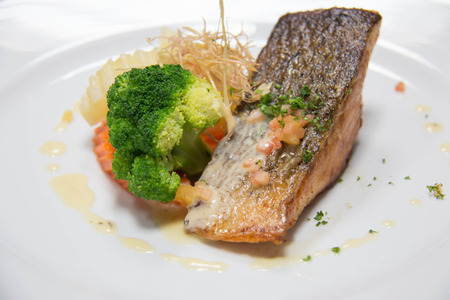 Tasty grilled salmon steak on mixedl vegetables with sauceの写真素材