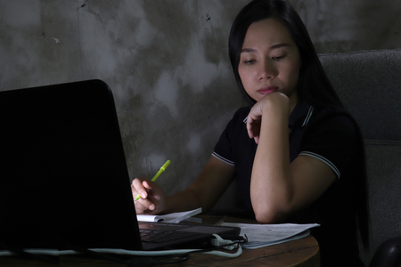 Asian woman working from home late at night Work in poor lighting concept. (dark light have some grain and noise)の写真素材