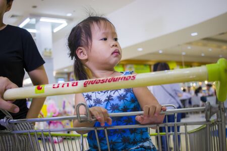 CHIANGMAI,THAILAND-MAY 3,2019 : Asian toddler girl looking for something and sitting in the trolley cart during family shopping in supermarketのeditorial素材
