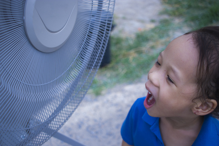 a children playing electric fan and enjoying cool wind in summer season High resolution image gallery.の写真素材