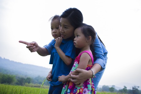 Happy Mother and her child play outdoors having fun, and pointing at something in the Green rice field. High resolution image gallery.の写真素材