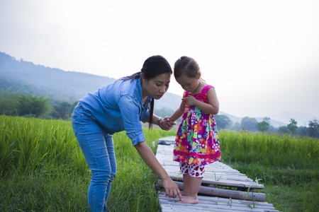Mother help her child to cross stream, mother lifting daughter in rice field.の写真素材