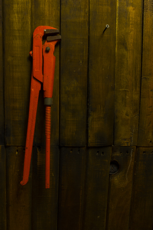 Old orange pipe wrench hanging on wooden wallの写真素材