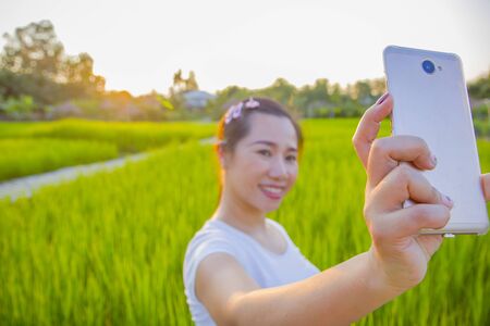 young happy and attractive Asian woman taking selfie portrait with internet mobile phone enjoying holidays of the sunset on the farmer's balcony in the rice fields  High resolution image gallery.の写真素材