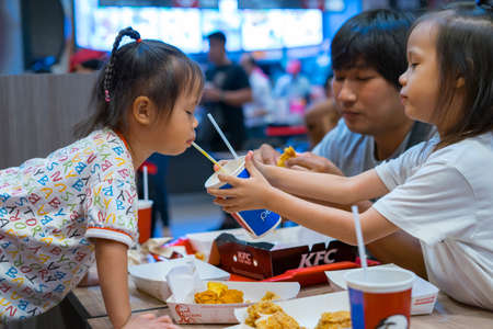 CHIANGMAI,THAILAND-Nov 14, 2019 : Little Child eating fried chicken with her family in the background of KFC (Kentucky Fried Chicken)restaurant.のeditorial素材