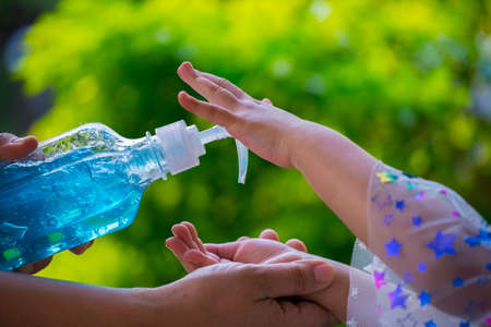 Blur background of mother cleaning her kids hand with alcohol gel sanitizer pump for hygiene protect weak ill chemotherapy, aids, kids patient from flu, germ, bacteria and virus covit-19 infection.の写真素材