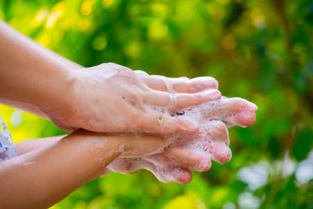 Mother and child washing hands with soap and water on green blur background.の写真素材