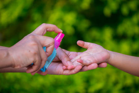 mother spry alcohol to cleaning her kids hand for hygiene protect weak ill chemotherapy, aids, kids...