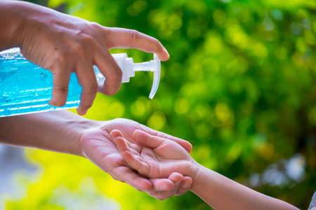 Blur background of mother cleaning her kids hand with alcohol gel sanitizer pump for hygiene protect weak ill chemotherapy, aids, kids patient from flu, germ, bacteria and virus covit-19 infection.の写真素材