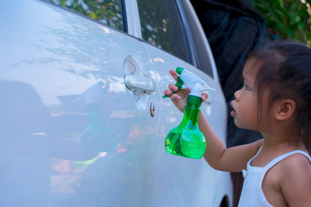 Asian children spry soap to clean car door handle.の写真素材
