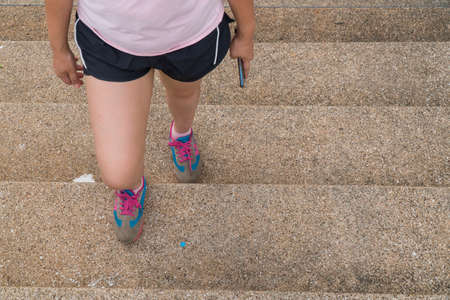 Portrait of asian chubby woman sitting on stairs of city street after running. Healthy runner resting after workout exercise. Active sporty woman enjoying outdoors in summer.の写真素材