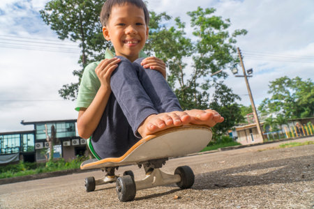 Asian little boy try to play skateboard stand and sit on it . Practice and practice to play.