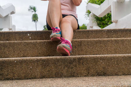 Portrait of asian chubby woman sitting on stairs of city street after running. Healthy runner resting after workout exercise. Active sporty woman enjoying outdoors in summer.の写真素材