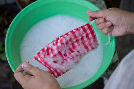 woman hand Washing a mask using detergent dissolved in water. Washing the masks is disinfecting and...