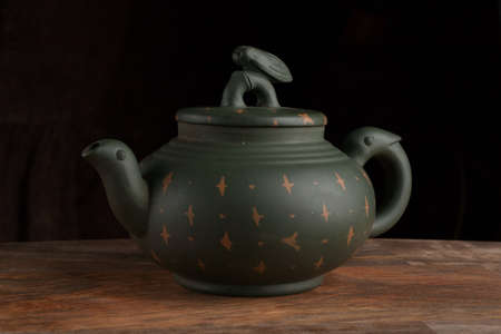 Green traditional chinese Yixin clay teapot with cicada on the cover. On the wooden table and black backgroundの写真素材