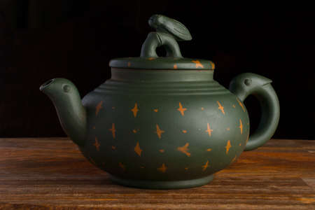 Green traditional chinese Yixin clay teapot with cicada on the cover. On the wooden table and black backgroundの写真素材