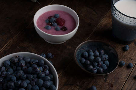 Glass of milk, cup of blueberries, cup of yogurt with berry and thistle branch on the old wooden tableの写真素材
