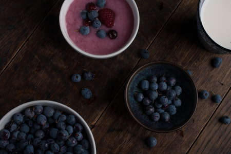 Glass of milk, cup of blueberries, cup of yogurt with berry and thistle branch on the old wooden tableの写真素材