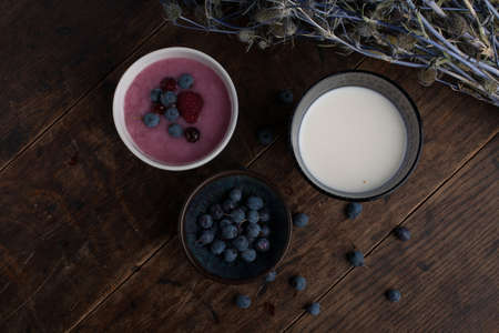 Glass of milk, cup of blueberries, cup of yogurt with berry and thistle branch on the old wooden tableの写真素材