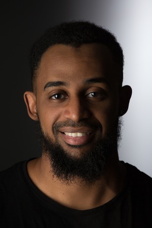 dark-skinned man smiles, photo straight look forward on a black and white background, with a beard...