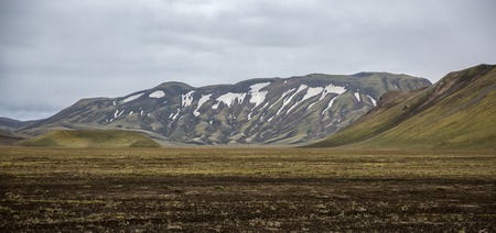 rugged green slopes of the volcanic hills of Iceland with snow capsの写真素材