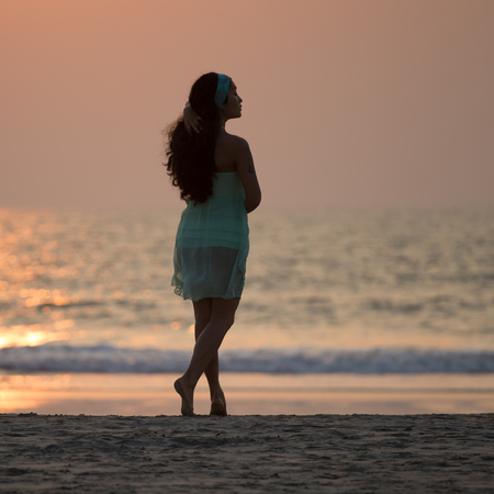 Silhouette of a beautiful girl standing on the beach at sunsetの写真素材