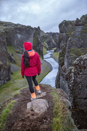 A girl in a red jacket stands on the edge of a deep gorge. A mountain river flows into the gorge. Picture taken in Iceland.の写真素材