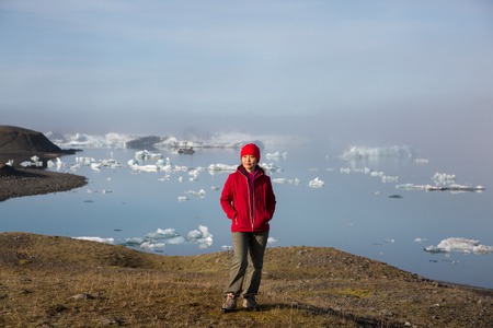 girl in a red jacket is standing at sunrise against the backdrop of a glasser lagoon in the fog.の写真素材