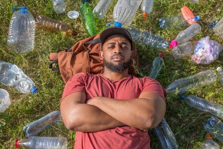 teenager dark skin lying on the grass surrounded by plastic garbageの写真素材